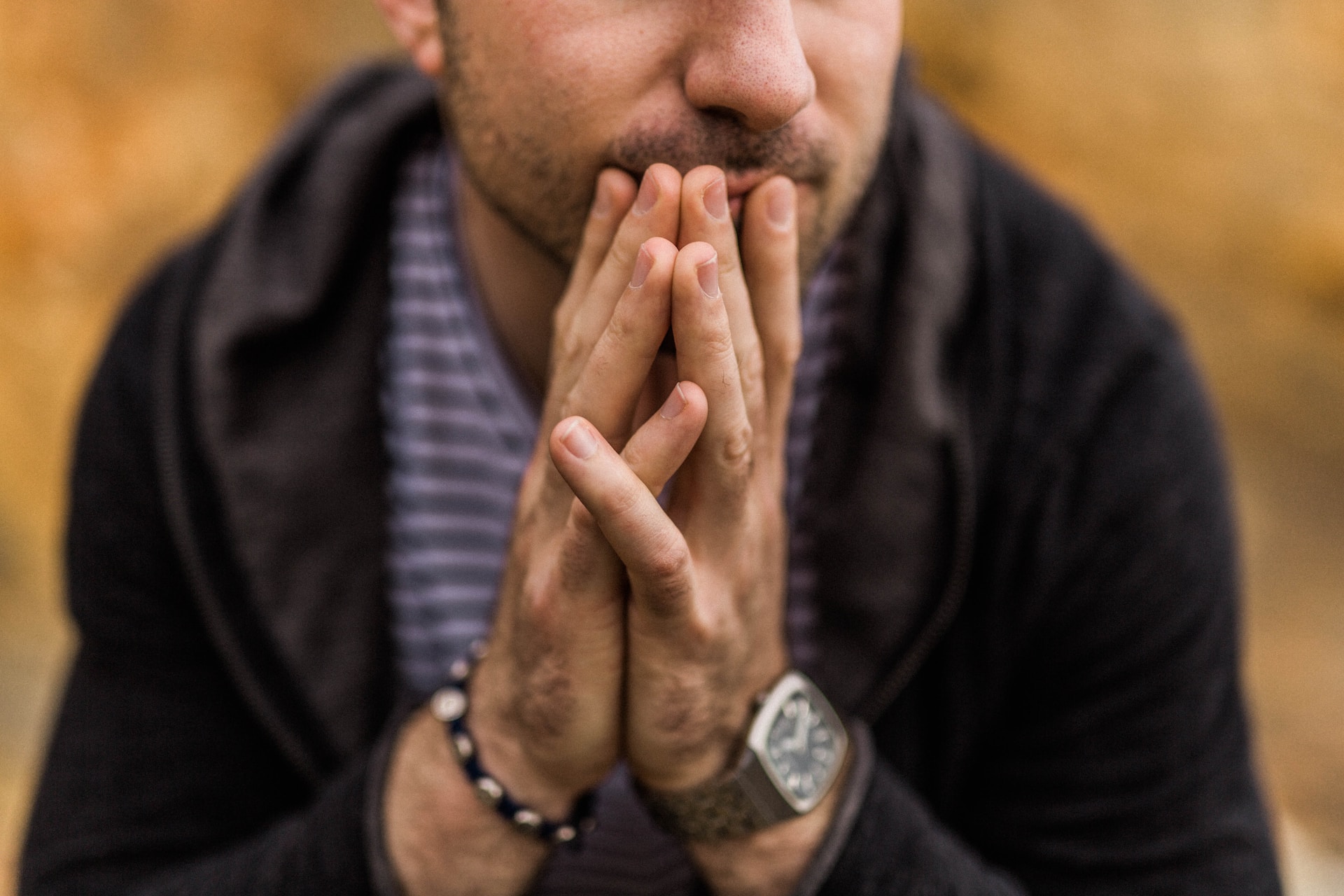 man sitting with hands together against his mouth thinking