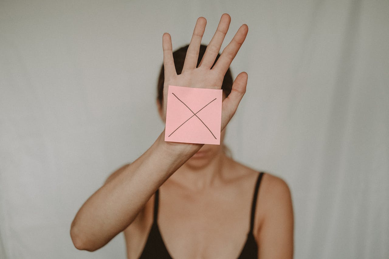 woman holding hand up in front of face with a paper on her palm with an 'x' on it